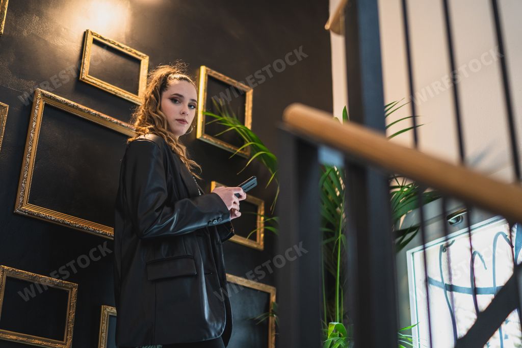 A young Caucasian woman looking at the camera by a wall with empty golden frames.