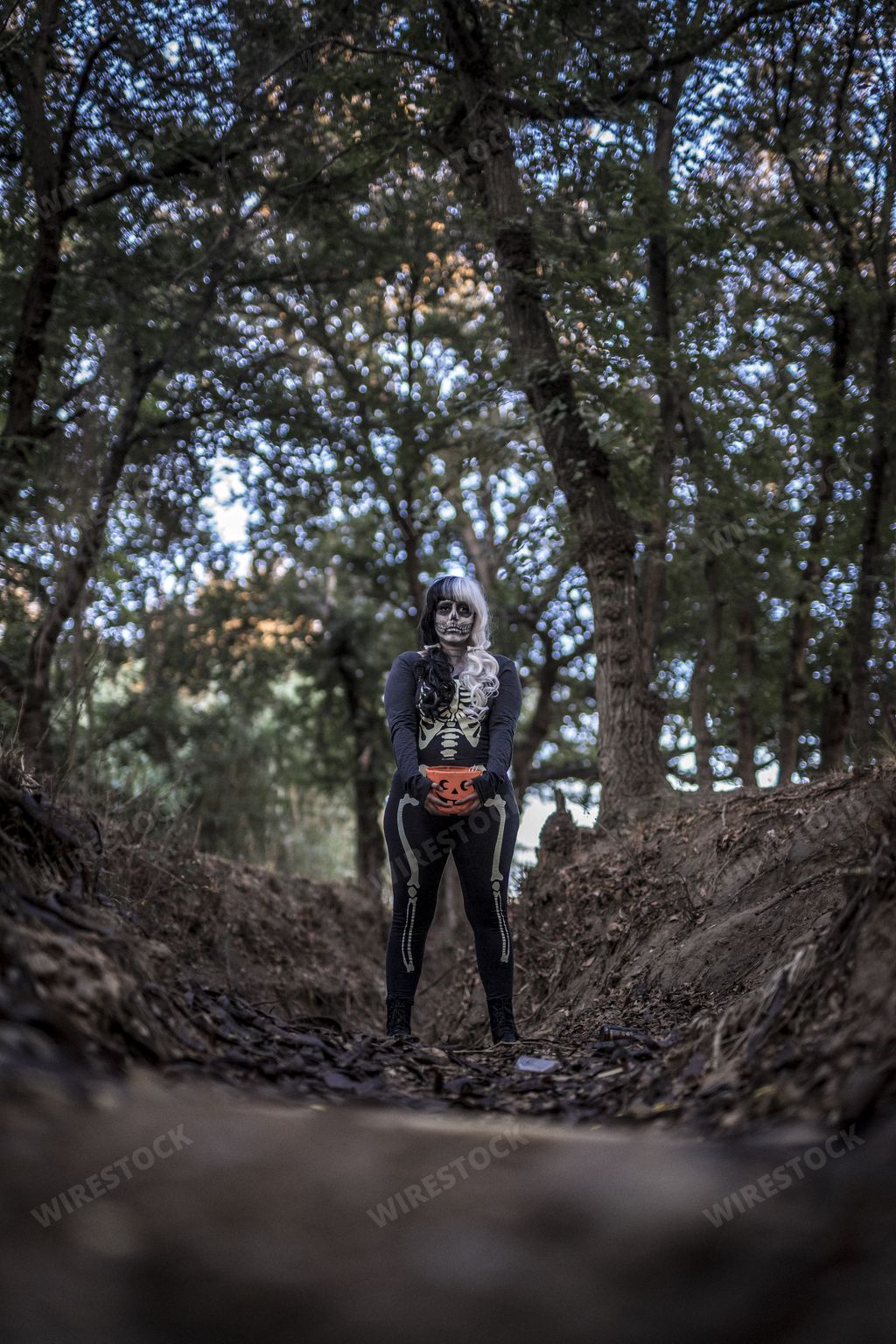 A vertical shot of a female wearing a skeleton costume and skull makeup in a creepy forest