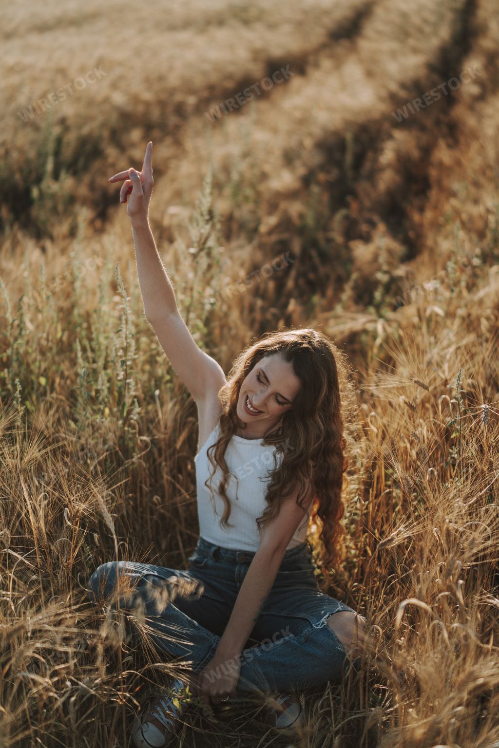 A beautiful Spanish girl enjoying her time alone with a smile and a stretched arm in a field