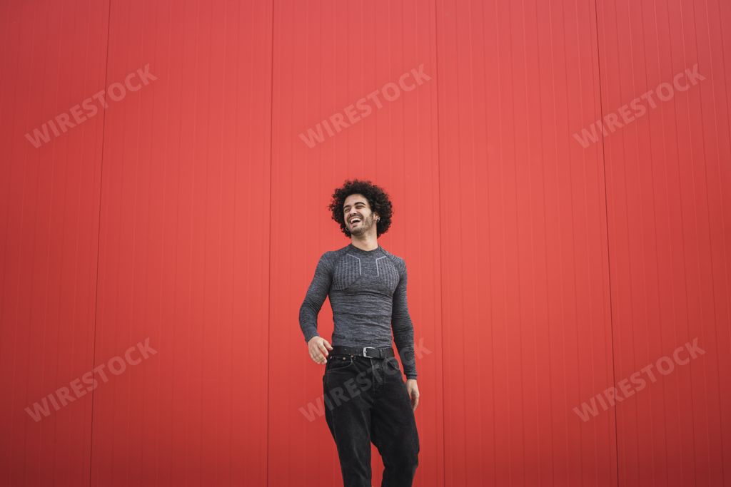 A happy stylish Spanish guy with curly hair posing in the red wall  background