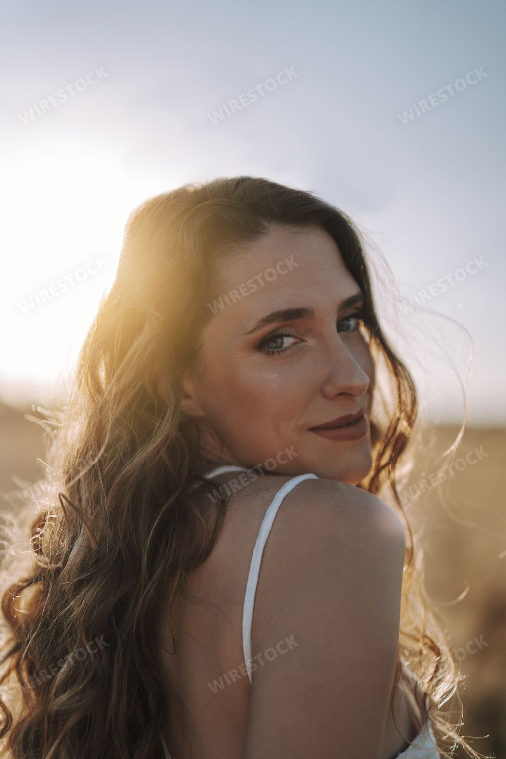 A vertical shot of a happy Spanish woman looking over her shoulder and smiling at the camera in a sunny field