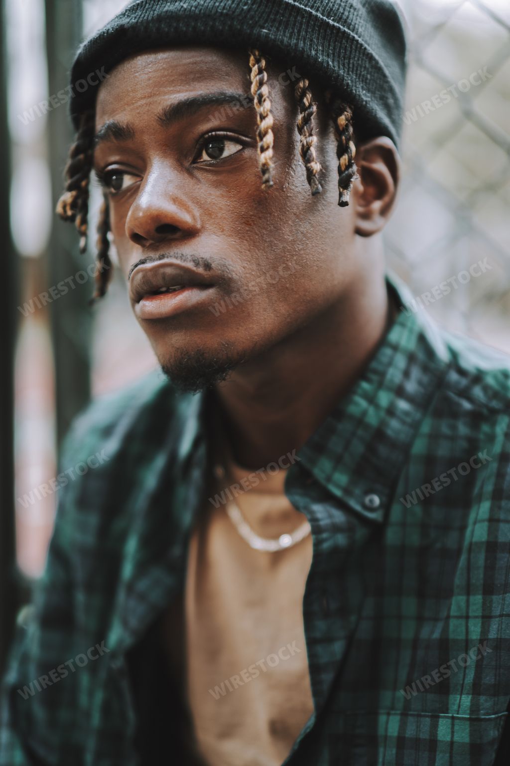 A handsome and stylish Spanish man posing with a chain-link fence on the background