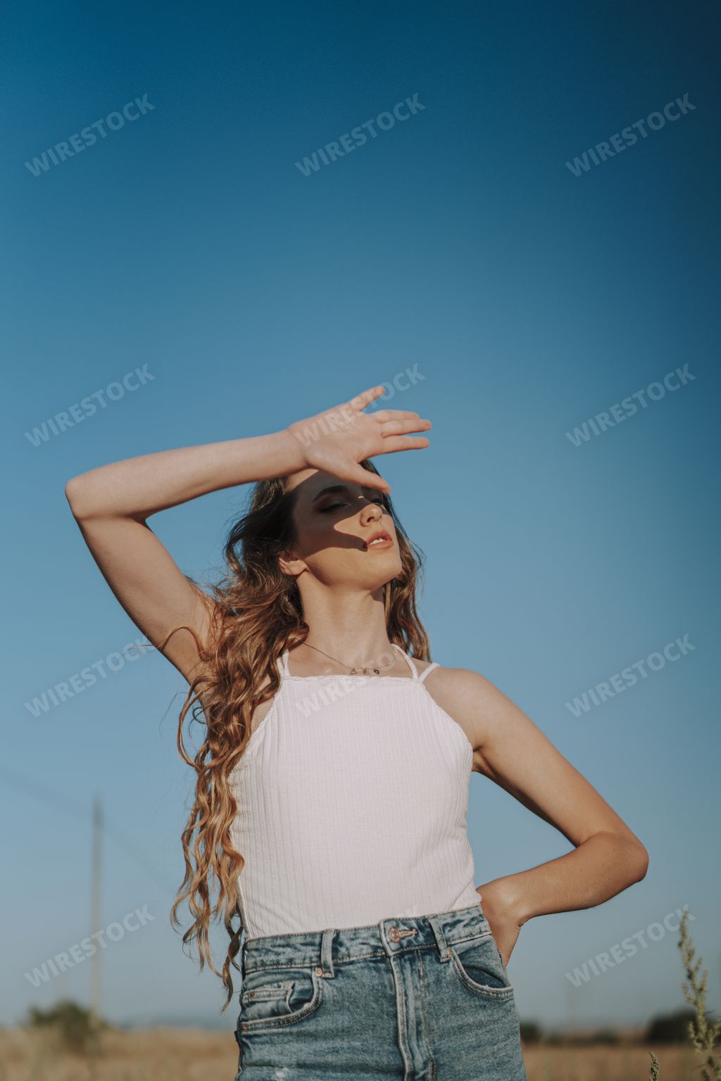 A vertical shot of a beautiful Spanish woman shielding her eyes from the sun with her hand in a wheat field