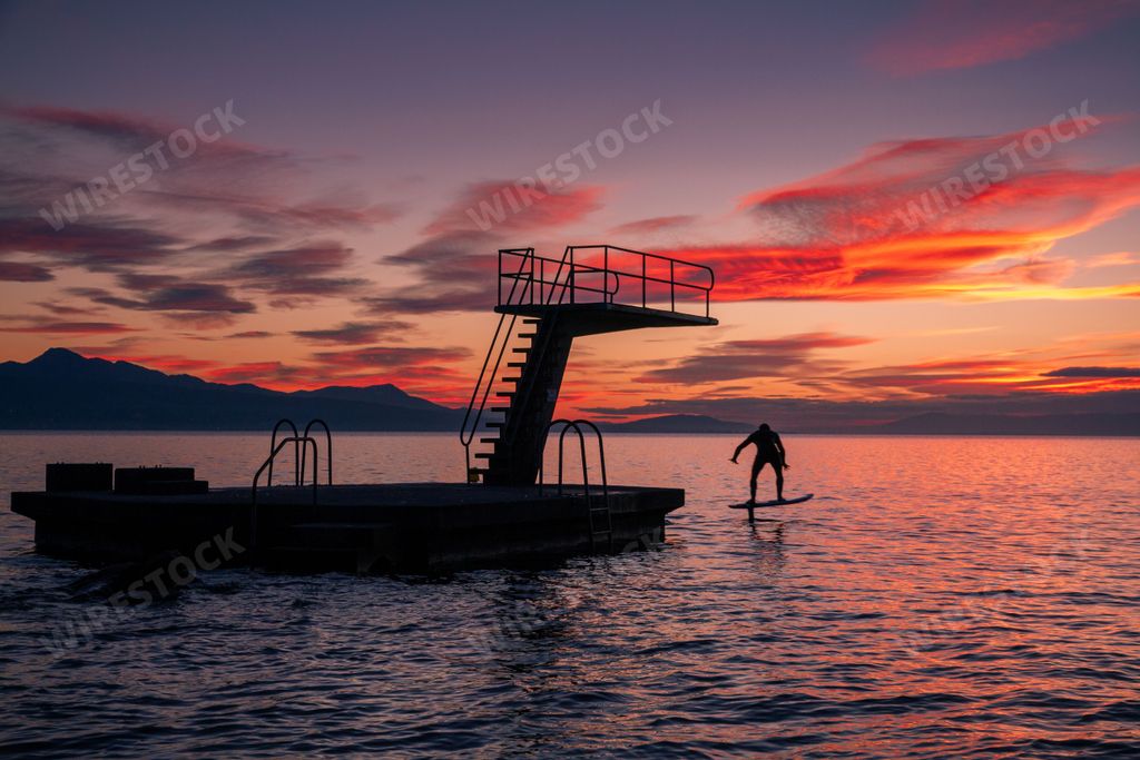 A mesmerizing pink sunset over the sea shore with a silhouette of a person foil surfing on the water