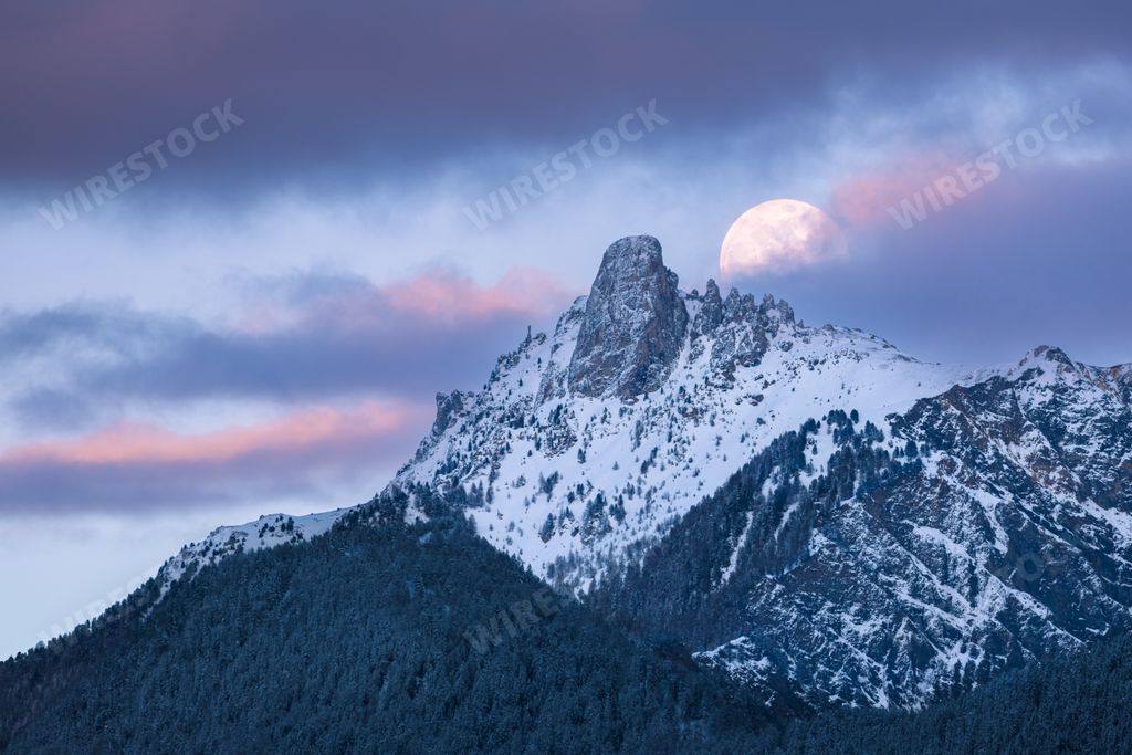 A beautiful view of the full moon partially covered over the Pierre Avoi mountain at sunset