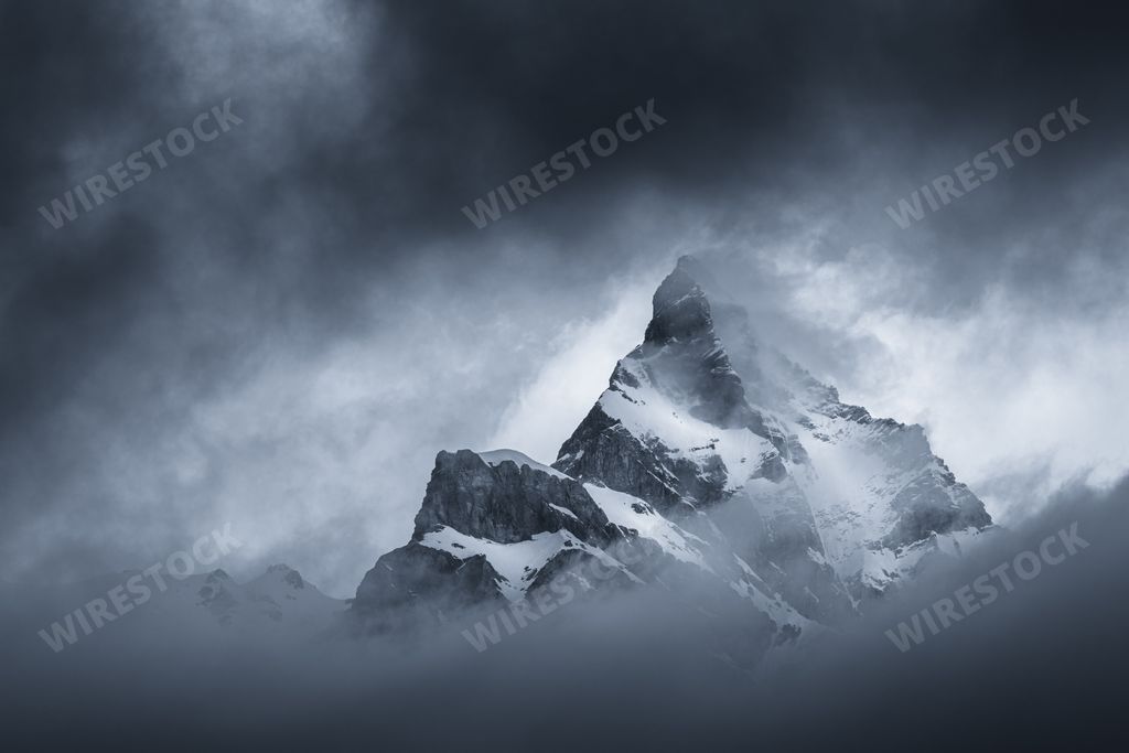 Moody black and white landscape view of a mountain appearing in the dark clouds at sunrise