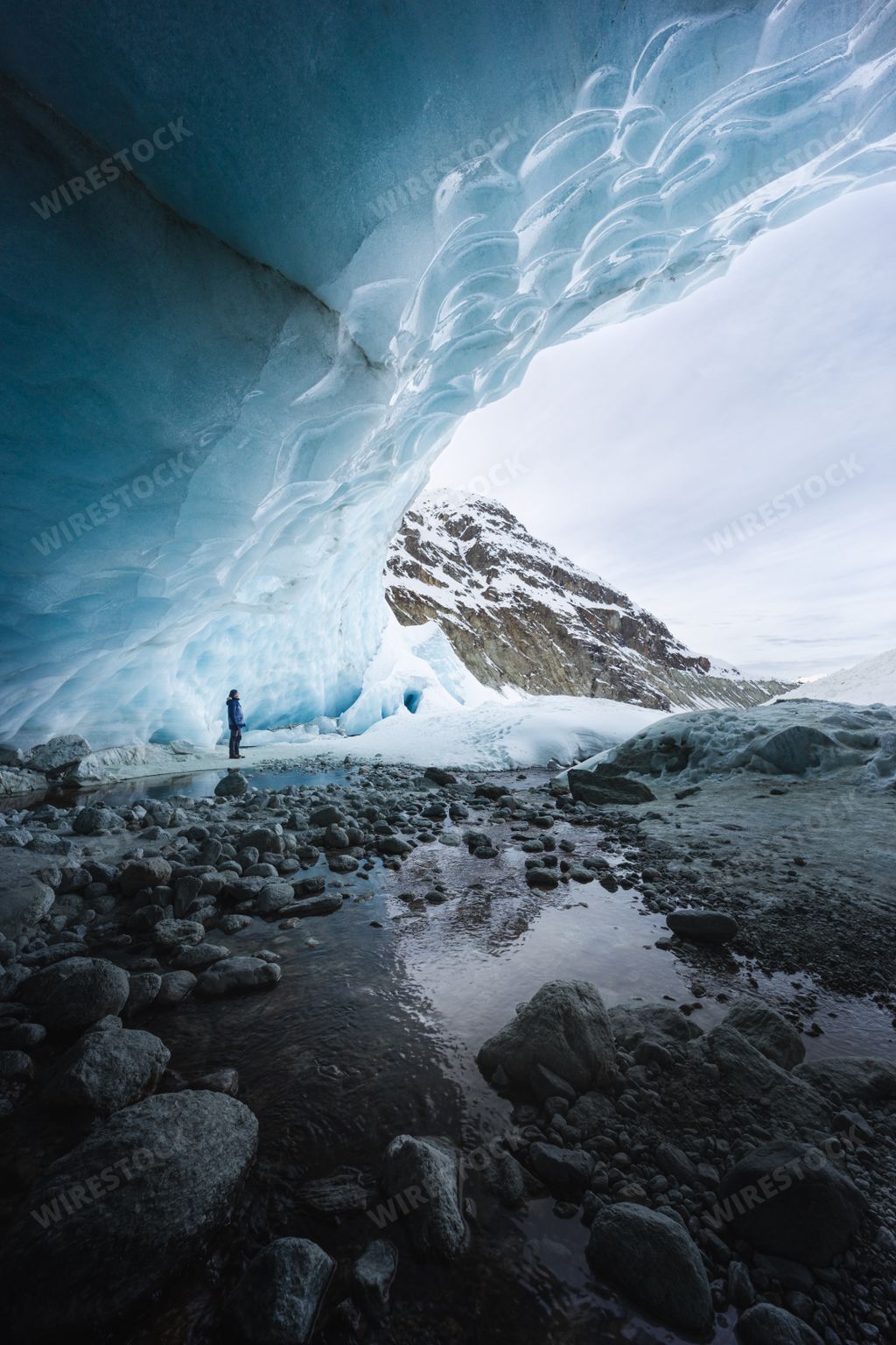 A vertical shot of the Zinal ice cave with a hiker looking at the ice above