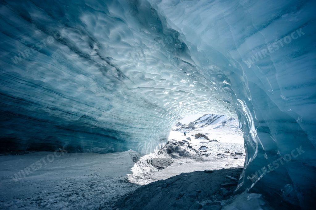 Ice cave in the Furgg glacier in Zermatt, Wallis, Switzerland, with the silouhette of a hiker, and blue shades and textures in the ice ceiling