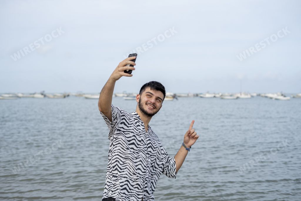 A Hispanic man taking selfies at a beach