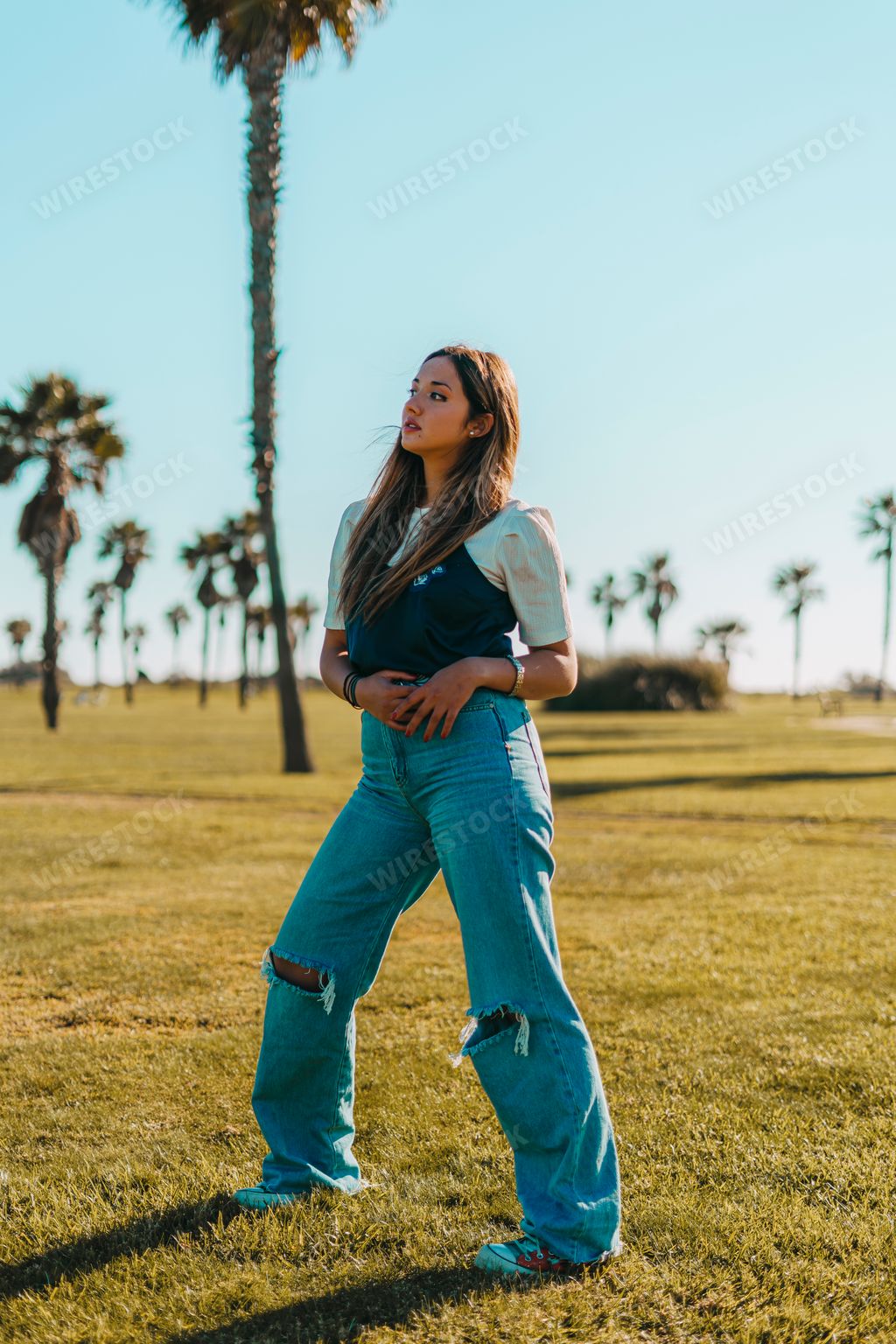 A Spanish fashion girl model in ripped jeans posing at the beach with palm trees in the background