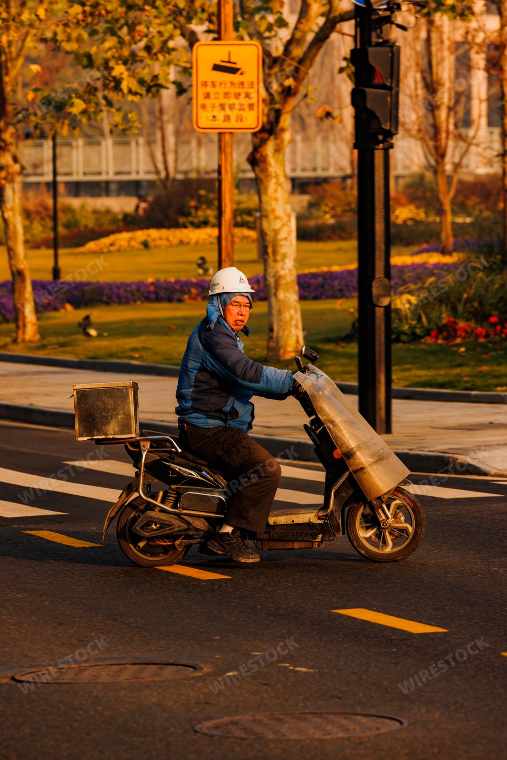A vertical shot of an Asian man in a helmet riding an old bike on a road in Shanghai, China