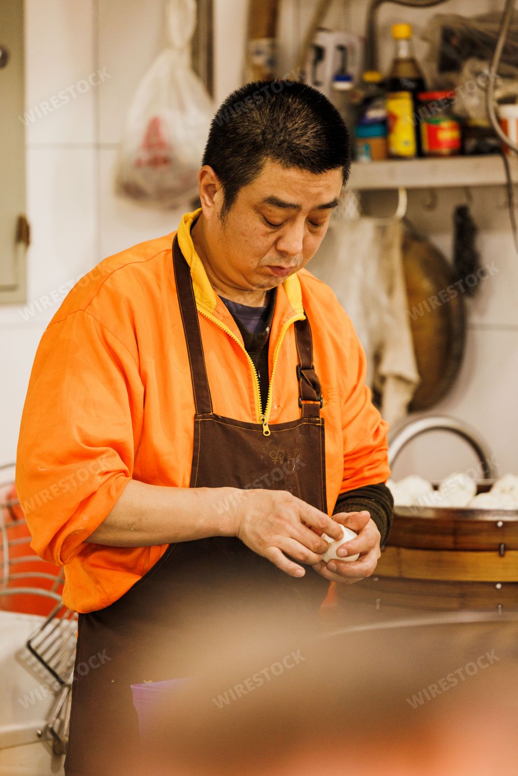 A vertical shot of an Asian man in an orange jacket with an apron working at a dumpling shop