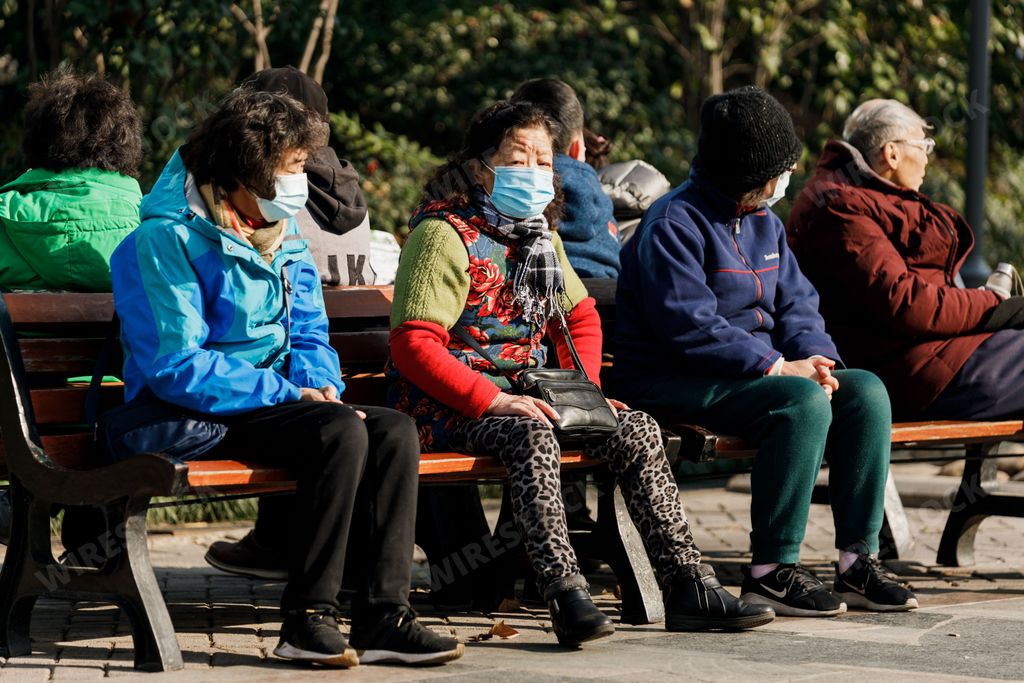 Some adult people sitting on a wooden bench in Shanghai.