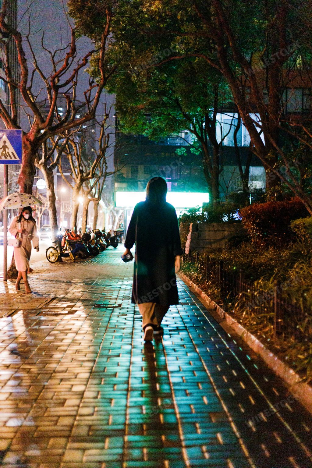 An Asian female walking on a sidewalk during nighttime, portrait