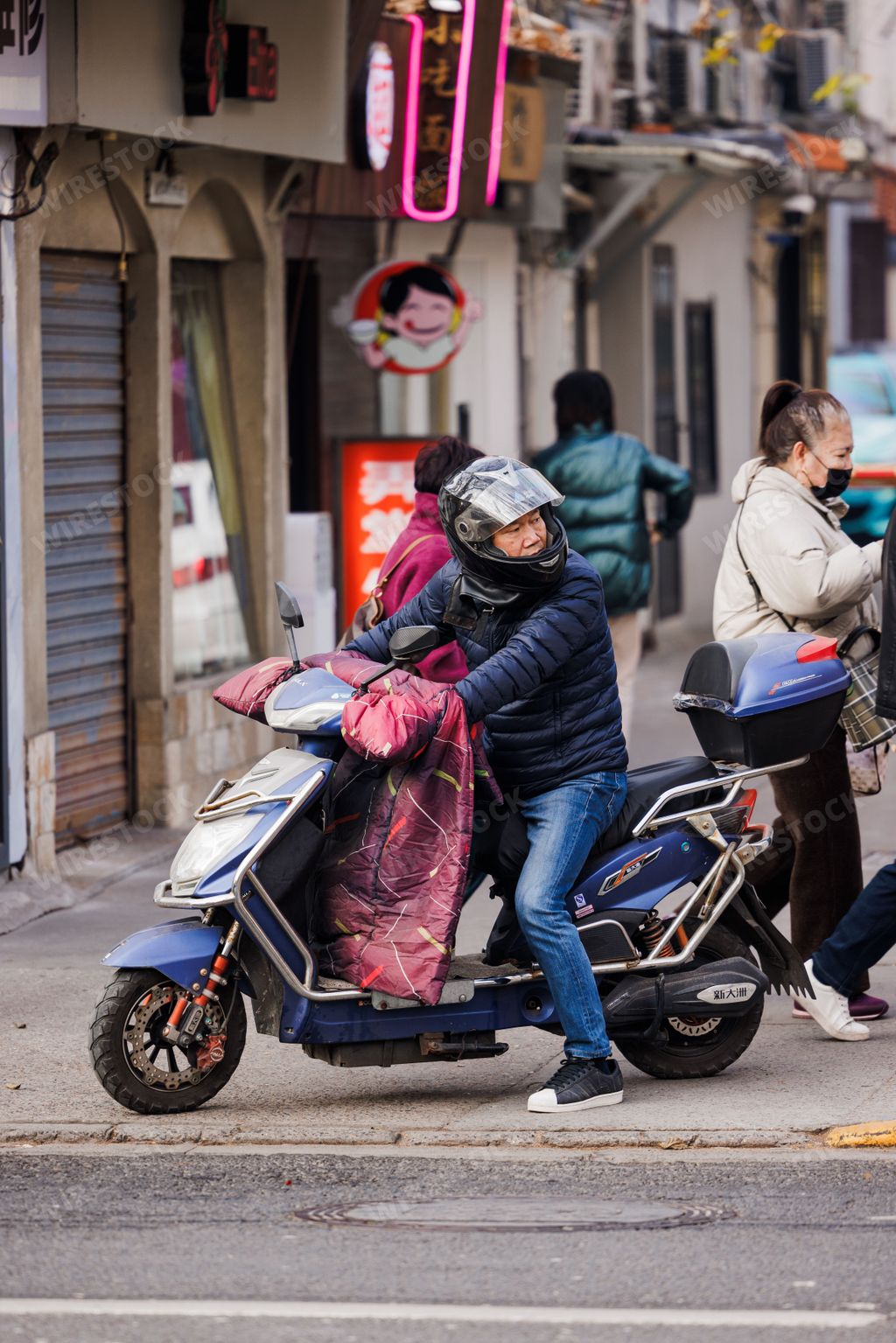 A vertical shot of an Asian man in a helmet riding a bike on a road in Shanghai, China