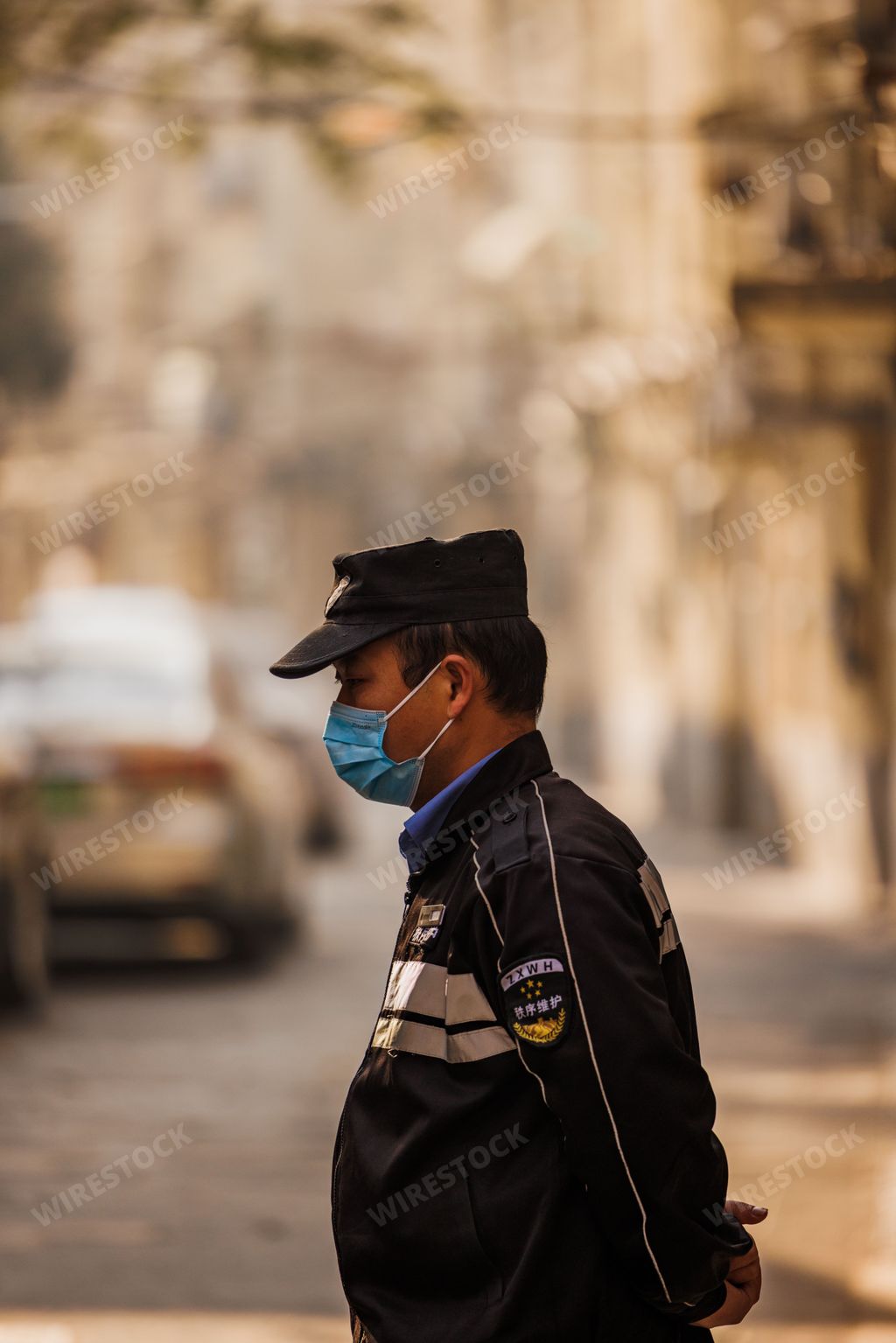 A vertical shot of a middle-aged Asian man in a mask and a cap in Shanghai, China