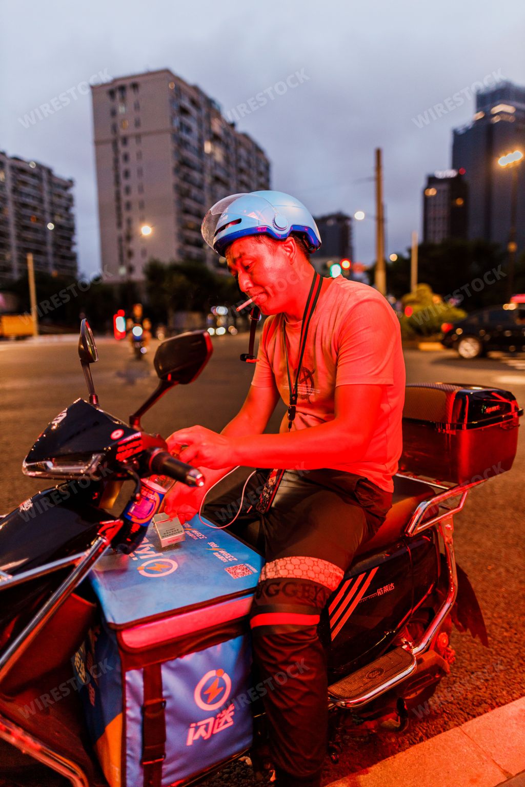 A vertical closeup of the man smoking on the scooter under red light. Selected focus. Shanghai, China.