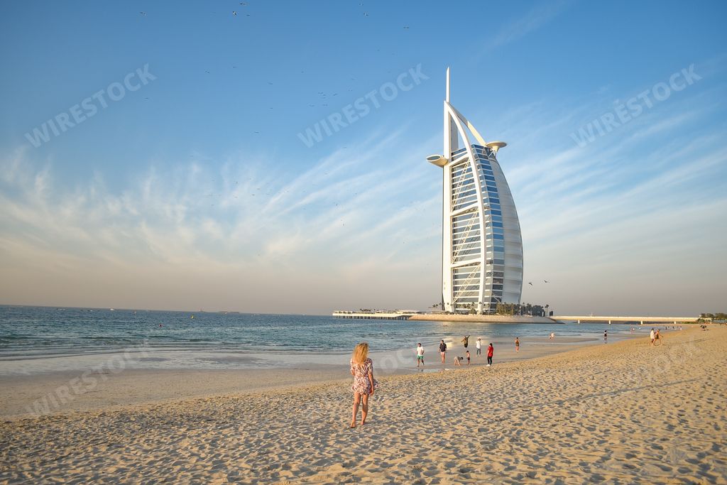 A back view of a young blonde female on Jumeirah Beach and luxury Burj al Arab hotel in background, Dubai, United Arab Emirates