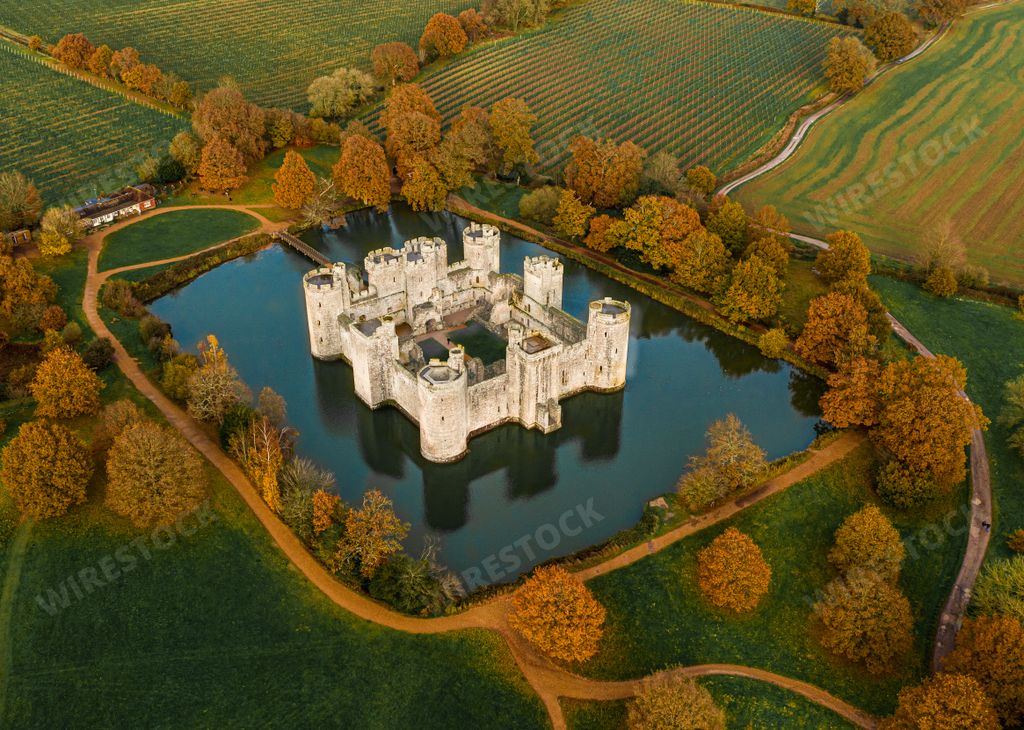 An aerial shot of a magnificent old castle in the middle of a lake surrounded by trees and farms