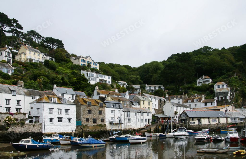 The sailing boats on the water and the houses on a tree-covered hill captured in Polperro Beach, UK