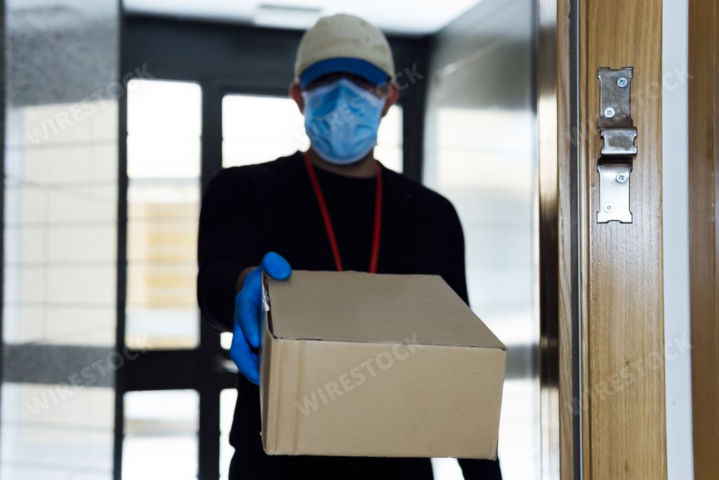 A male in a face mask and plastic gloves delivering an order during the COVID-19 pandemic