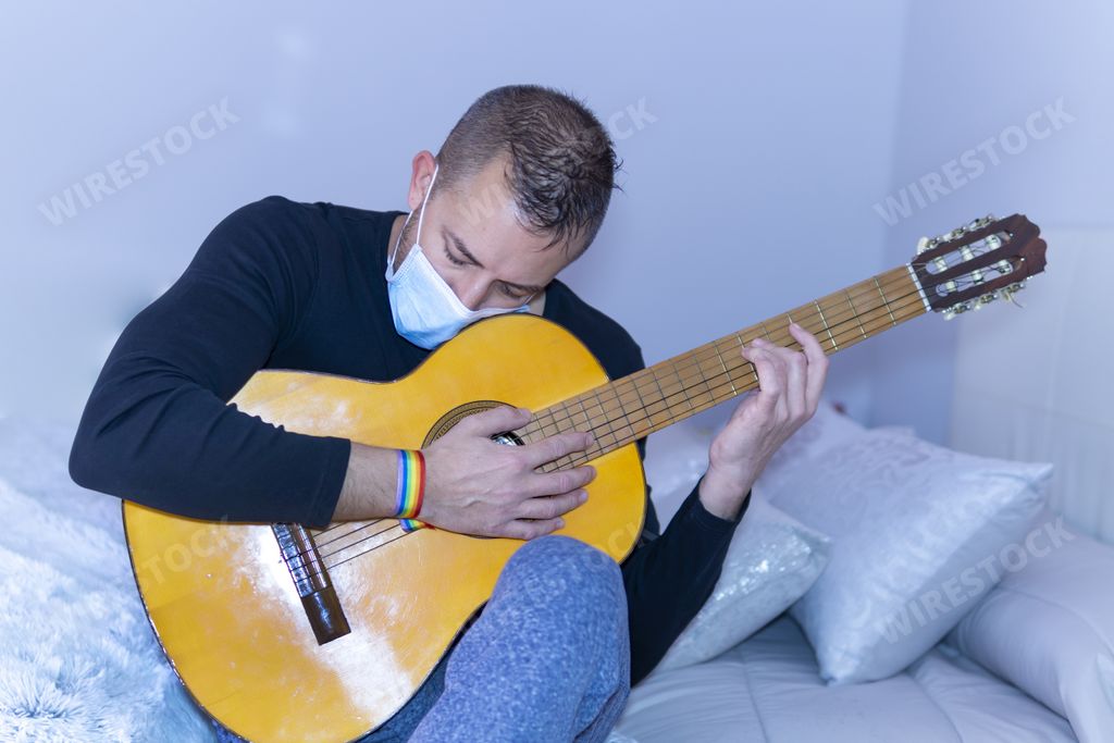 A closeup shot of a young male wearing medical face mask and playing guitar