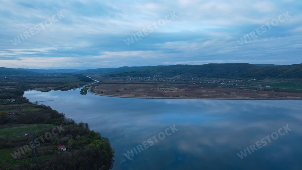 An aerial shot of a wide river near a greenfield