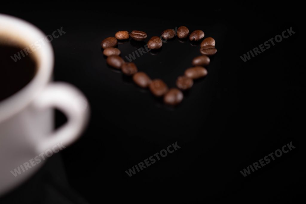 A heart made of coffee beans and a cup of espresso on a black background